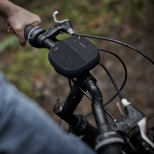 Person holding bike handlebars with a speaker mounted on them.