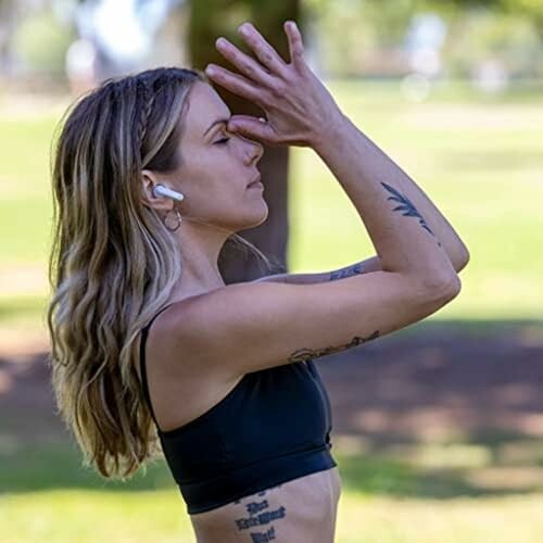 Woman practicing yoga outside wearing wireless earbuds.